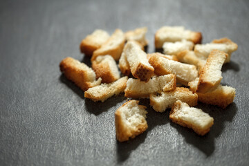 Baked dry pieces of white bread, crackers, on dark background, selective focus.