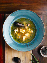 Transparent fish soup with pieces of red salmon fish, trout in a blue bowl on a wooden background. The concept of healthy eating. Close up. Space for text. Fish dish, lunch. Soup with mussels.