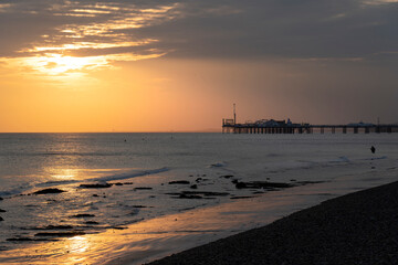 Fisherman against golden sunset with Brighton Pier in background.