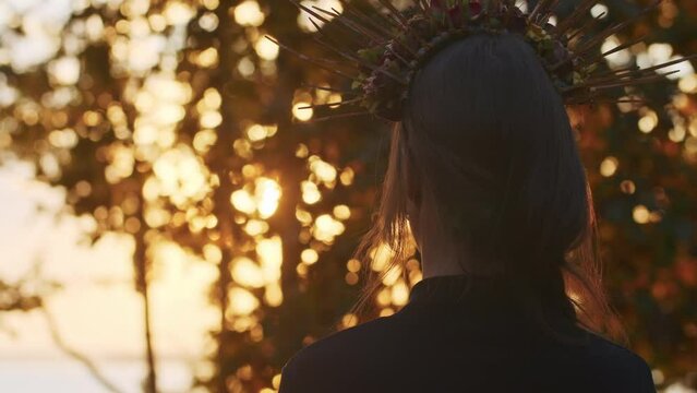 A young woman with Santa Muerte make-up dressed in a black dress of death walks against the backdrop of autumn leaves in the forest during sunset. Day of the Dead or Halloween concept.