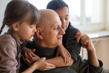 grandfather and two granddaughters hugging on sofa at home