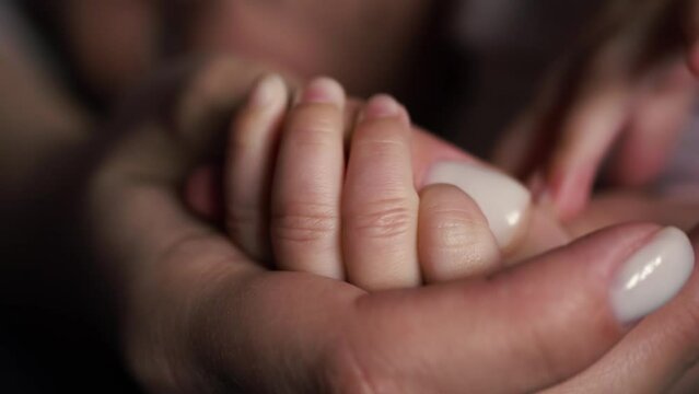 The baby squeezes the hand, the thumb of mom, with a white manicure, with small fingers. Soft skin.