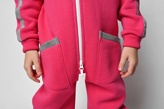 Close-up of a child in a bright pink fuchsia jumpsuit with a zipper and pockets on a light background. Pockets, cuffs, pants, legs