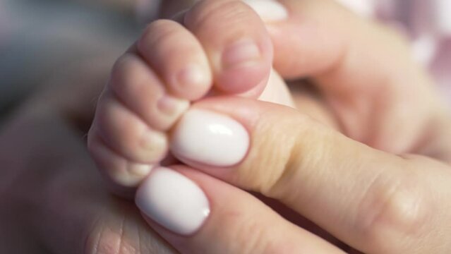 Close-up. The baby squeezes the toes when the mother tickles the skin of the heel. White manicure, day. Static camera