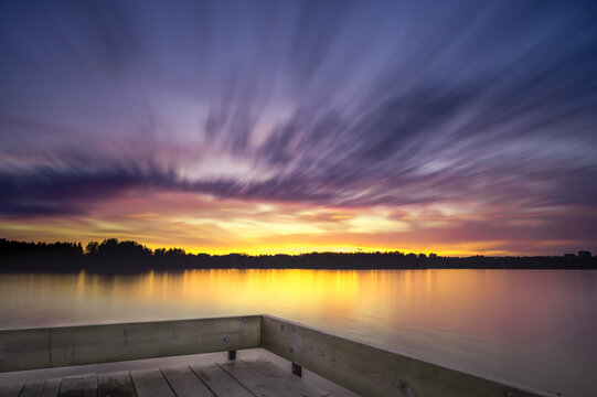 Panoramic Tranquil golden hour cloud above the forest lake at sunset. Dramatic cloudscape. Long exposure on the water