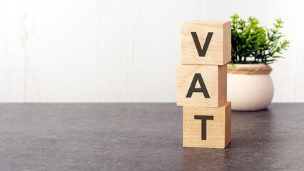 letters of the alphabet of VAT on wooden cubes, green plant, white background
