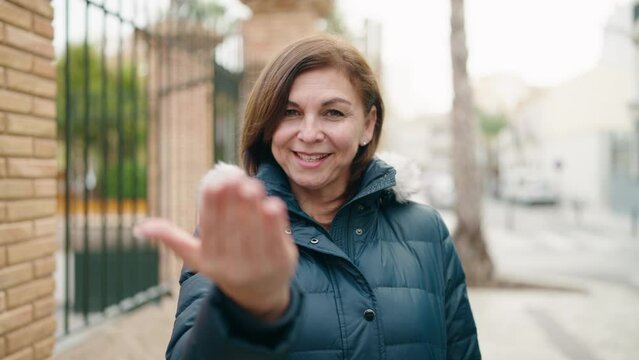 Middle age woman smiling confident doing coming gesture with finger at street