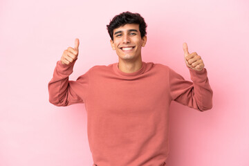 Young Argentinian man isolated on pink background giving a thumbs up gesture