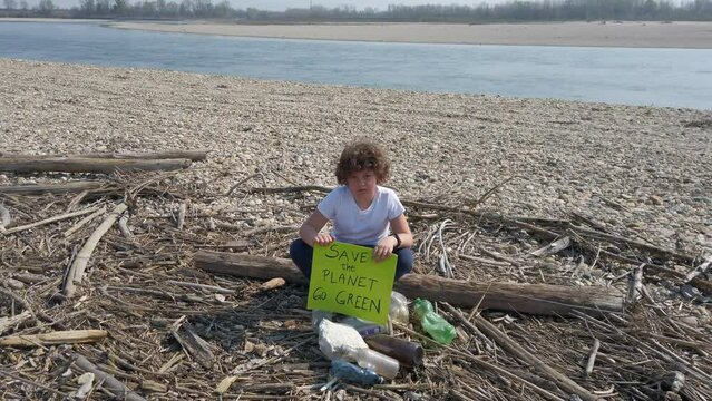 7-year-old boy protests with the inscription Save the Planet go green, against climate change and global warming near the Po river in drought without water with plastic bottle pollution 