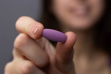 Closeup of a woman holding a purple multivitamin pill.