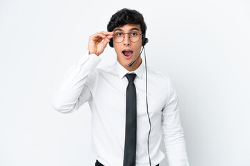 Telemarketer man working with a headset isolated on white background with glasses and surprised