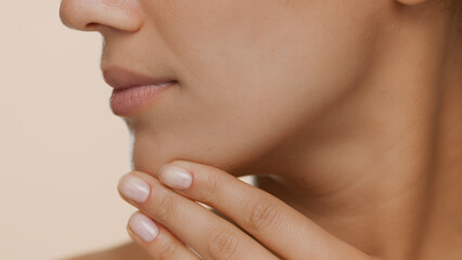 Extreme close-up shot of young woman with perfect skin strokes her jaw line and chin on beige background | Smooth skin and beauty care commercial concept