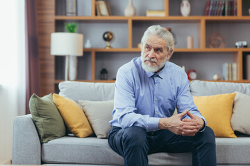 Serious for pensive grandfather man sitting on sofa at home - Powered by Adobe