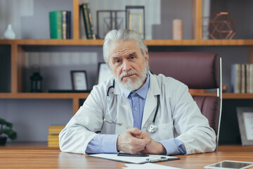 Portrait of a senior experienced doctor gray-haired man working in the office, looking at the...