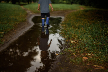 Boy in a blue T-shirt and blue rubber boots walks through a puddle