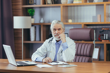 Portrait of a senior experienced doctor gray-haired man working in the office, looking at the camera