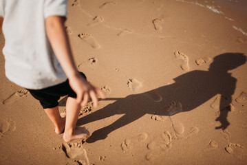 A boy walks on the beach, leaving footprints in the sand