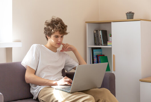Cute young teenager with laptop on the couch at home. Boy makes homework with a computer. Distance, online education for children
