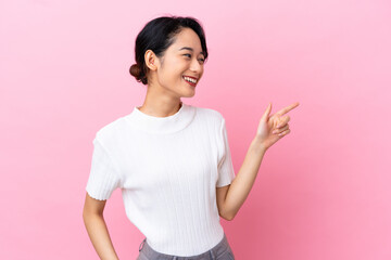 Young Vietnamese woman isolated on pink background pointing finger to the side and presenting a...