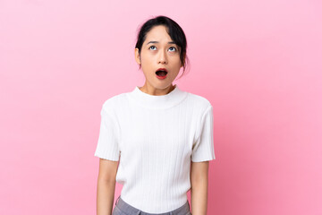 Young Vietnamese woman isolated on pink background looking up and with surprised expression