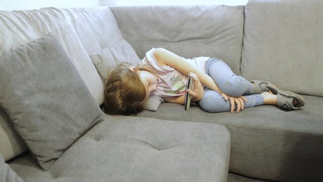 a little girl is lying on the couch and watching cartoons on the phone screen