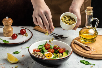 Woman mixing delicious superfood salad quinoa, avocado, egg, tomatoes, spinach and sunflower seeds on light background. Healthy food, ketogenic diet, diet lunch concept, place for text, top view