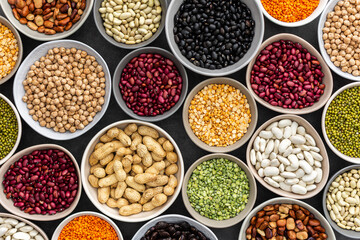 Different types of legumes in bowls, green with yellow peas and mung beans, chickpeas and peanuts, colored beans and lentils, top view