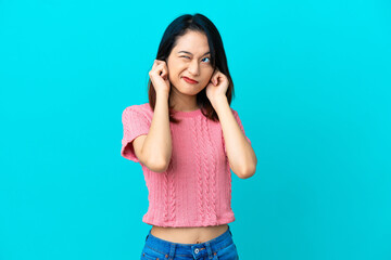 Young Vietnamese woman isolated on blue background frustrated and covering ears