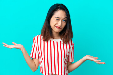 Young Vietnamese woman isolated on blue background having doubts while raising hands