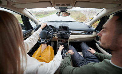 Back view of happy man and woman traveling in car. Young couple sitting on front passenger seats, beautiful woman driving comfortable automobile.