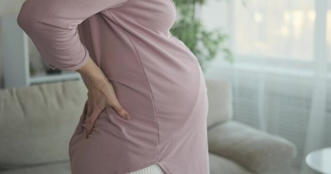 Woman caressing her pregnant belly and stretching while massaging her lower back