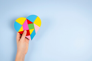 Child hand holding colorful puzzle heart on light blue background. World autism awareness day concept