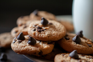 Chocolate chip cookies on a white plate, with a cold glass of milk on the side, over a wooden table. Horizontal Macro photography