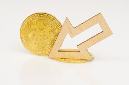 On a white surface, bitcoin and an arrow showing a decrease in the value of the cryptocurrency.