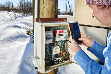 Reading electricity meter in outdoor switchboard in winter, using smartphone.