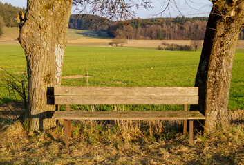 a view with an old wooden bench in the German countryside on a sunny spring day in Birkach, Bavaria (Germany)	
