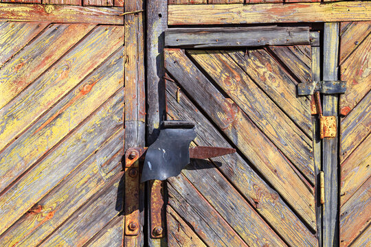 Old wooden stable gate of the boards with shabby paint. Fragment of closed wooden gate with rusty hinges, closeup