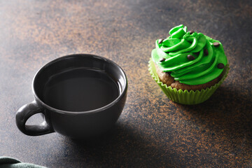 St. Patrick's Day coffee and chocolate cupcake with green whipped cream on brown background. Close up.