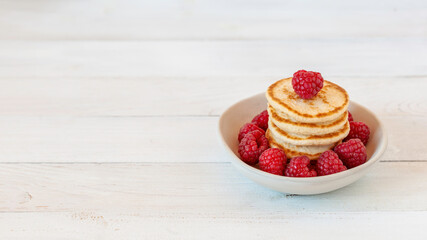 Stack of pancakes decorated with raspberries in a bowl, wooden background