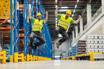 Two warehouse workers jumping and celebrating success. - obrazy, fototapety, plakaty