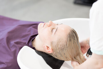 Professional hairdresser washing beautiful young woman's hair in the salon. Beauty procedure. Self care