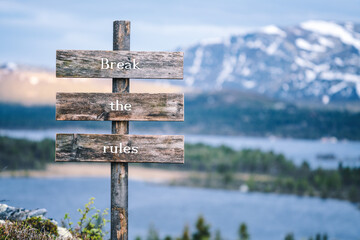 break the rules text quote written on wooden signpost outdoors in nature with lake and mountain scenery in the background. Moody feeling.