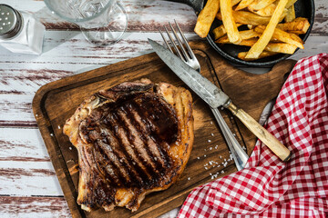 Incredible juicy t-bone cooked on the grill or barbecue on a wooden board accompanied by a french...
