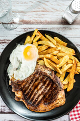 Plate with a juicy t-bone grilled or barbecued, accompanied by a portion of french fries and a fried egg. Traditional, homemade food concept. vertical orientation.