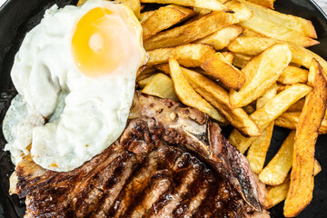 Plate with a juicy t-bone grilled or barbecued, accompanied by a portion of french fries and a...