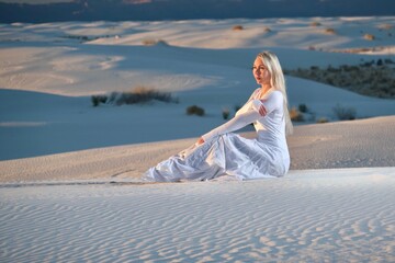 Fototapeta na wymiar Woman in white dress sitting on white sand at sunset. White sands. Alamogordo. New Mexico. United States of America