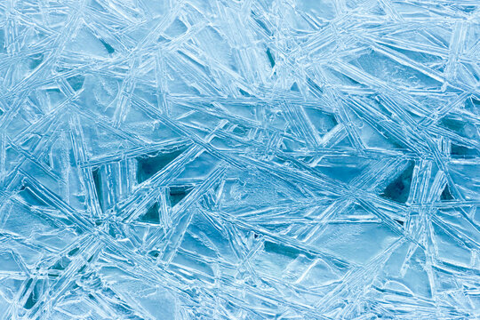 Texture frozen natural blue ice crystals closeup, top view. Ice patterns on the water surface winter. Natural ice background