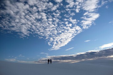 Serene morning white clouds on blue sky. Couple walking holding hands on white sand. New Mexico. United States of America 