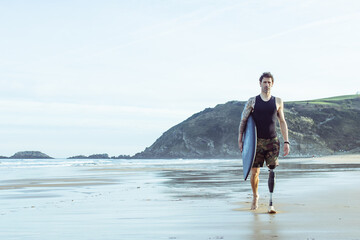 Caucasian surfer man, seen from front, walking along the beach with an artificial leg.Copy Space