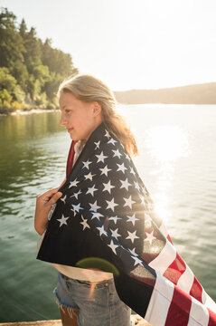 Side View of Young Girl Wrapped in American Flag on Sunny Evening
